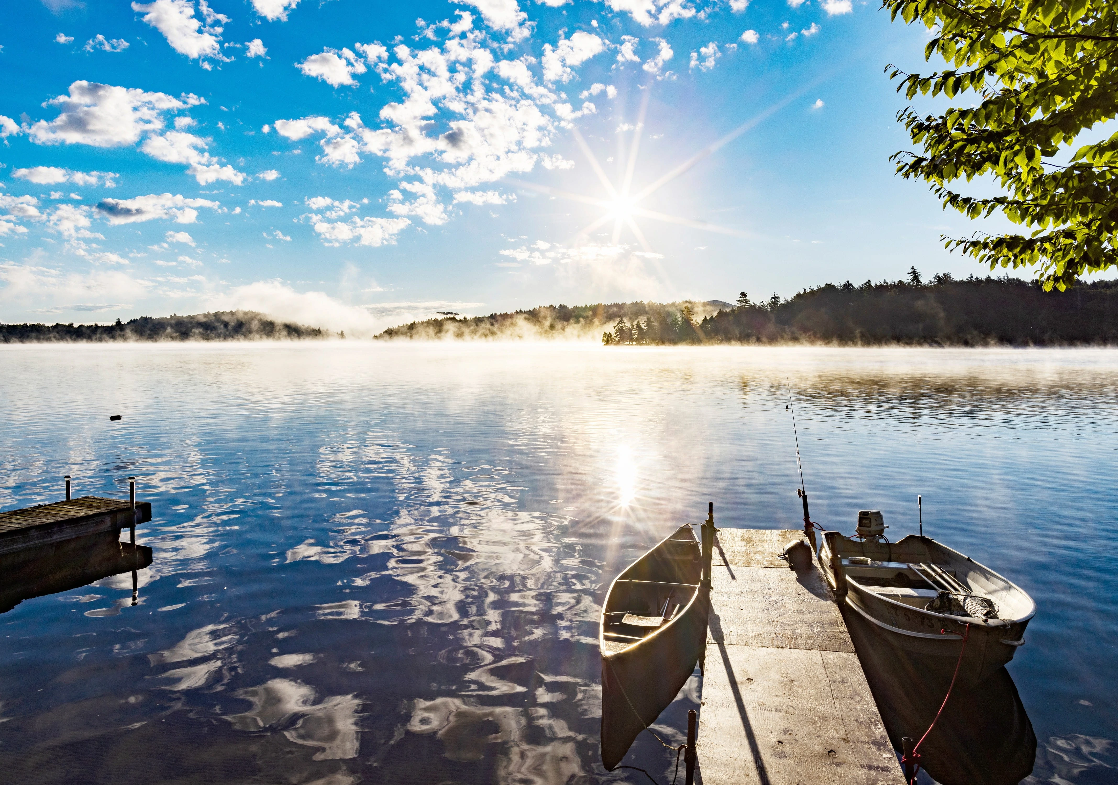 Canoe, rowboat tied to a dock on Upper Saranac Lake, NY in bright morning sun and mist