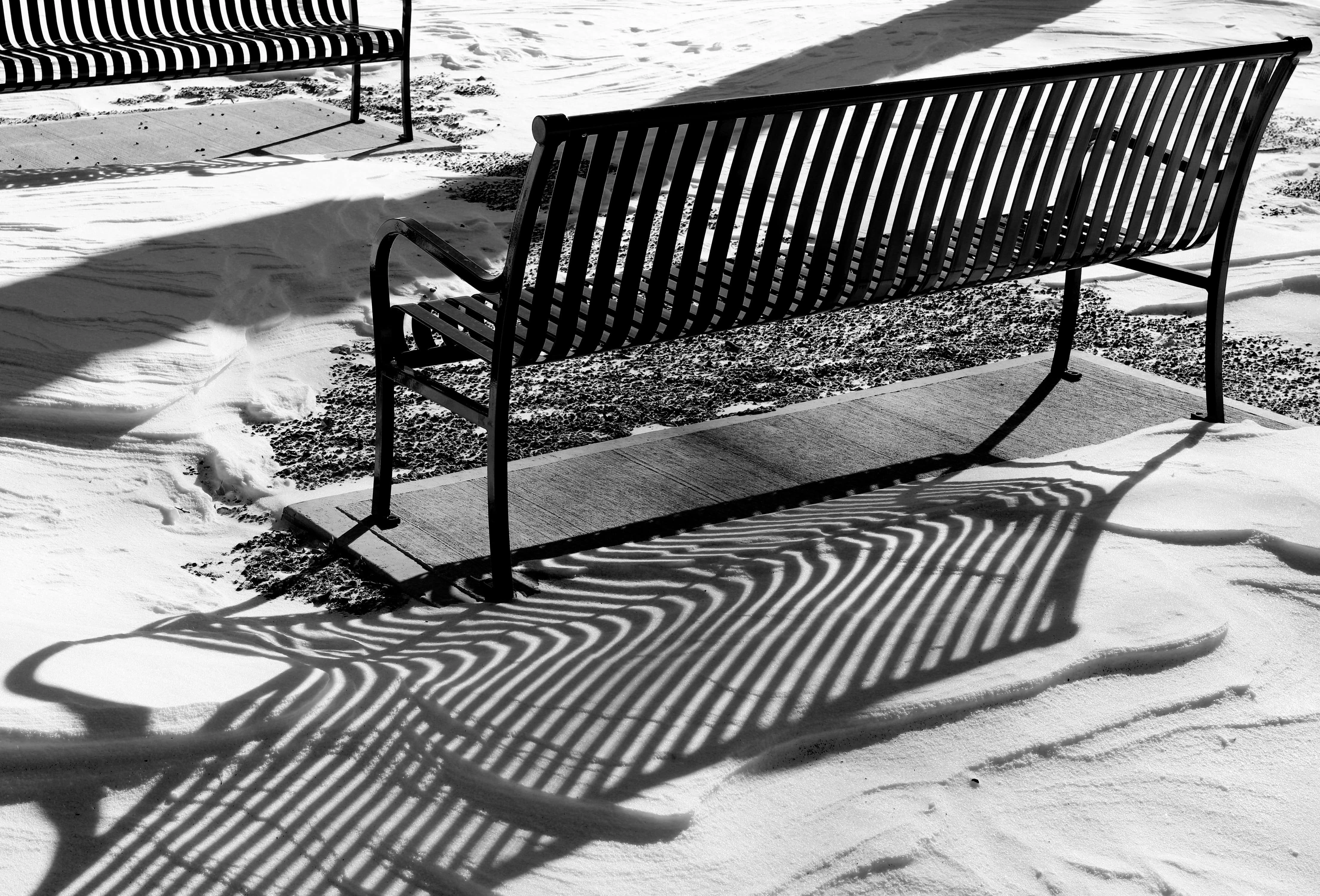 Two park benches in bright sunshine and snow covered ground