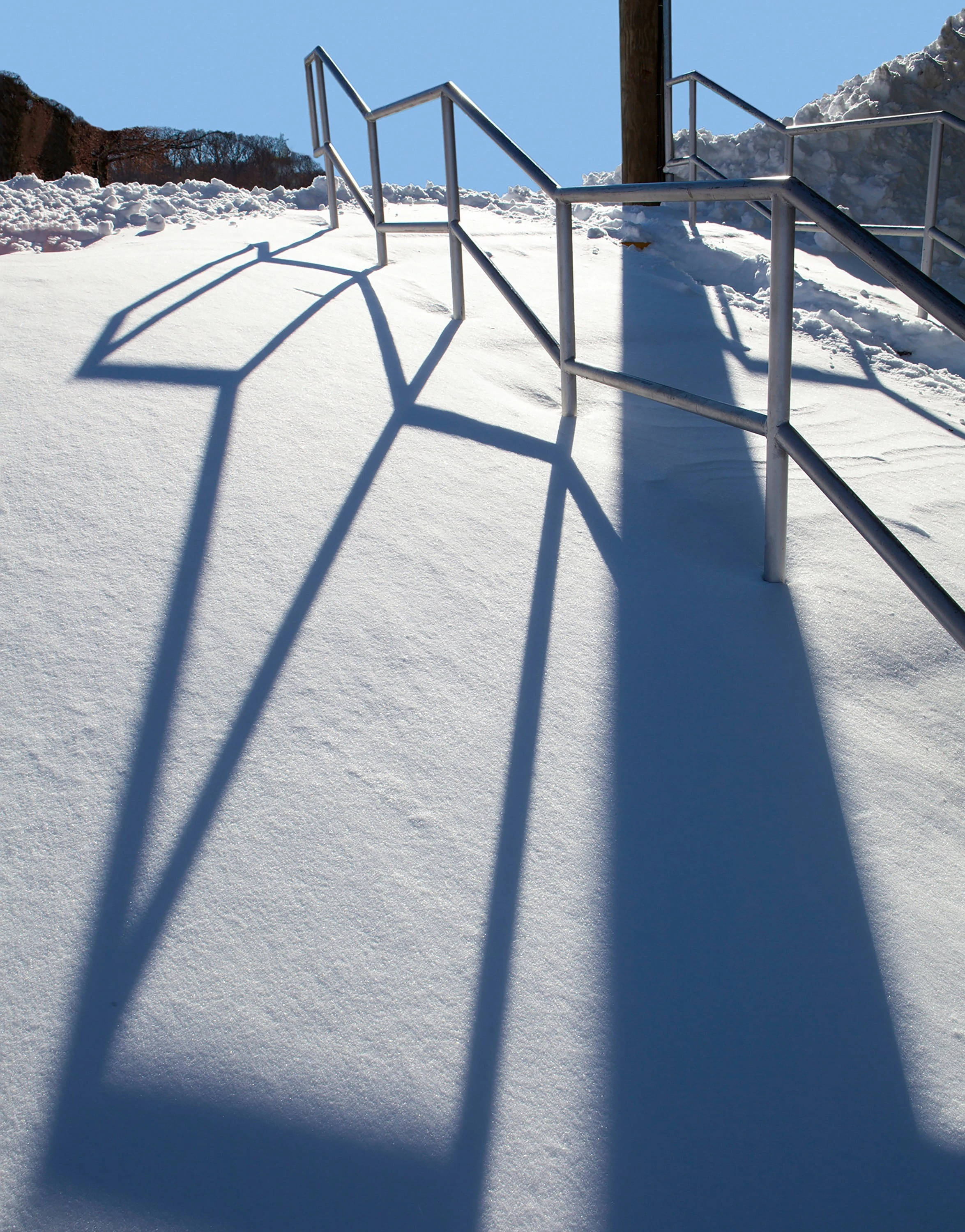 Staircase rails in deep snow with strong shadows, blue sky